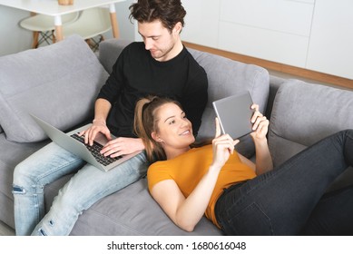 Couple Using Fast Home Internet With Laptop And Digital Tablet. Woman And Man On Sofa In Living Room