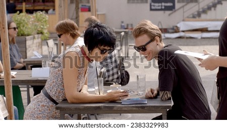 Couple using his phone during the date. Checking messages, browsing the internet, or using it as a conversation starter or to share something interesting with girl. People lifestyle.