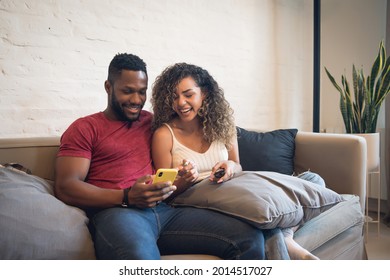 Couple Using A Mobile Phone While Sitting On A Couch At Home.