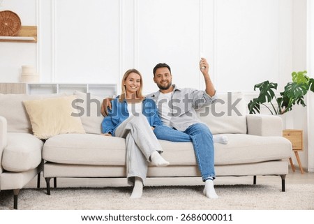 Couple using remote to control air conditioner on sofa at home