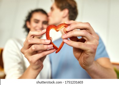 Couple Of Vegetarians Making Heart With Sliced Pepper While Preparing Healthy Meal In The Kitchen Together. Guy Kissed His Girlfriend. Vegetarianism, Healthy Food Concept. Main Focus On Hands