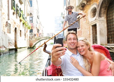 Couple In Venice On Gondola Ride Romance In Boat Happy Together On Travel Vacation Holidays. Romantic Young Beautiful Couple Taking Self-portrait Sailing In Venetian Canal In Gondola. Italy.