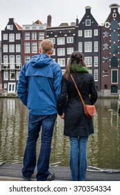 Couple Waiting On Pontoon For A Boat Ride In The Old Of Amsterdam City Center 