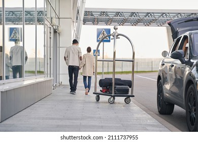 Couple Walking Along Airport Building Before Baggage Cart