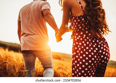 Couple walking along the wheat field holding hands on a sunny day. Light backdrop. Wheat field.
