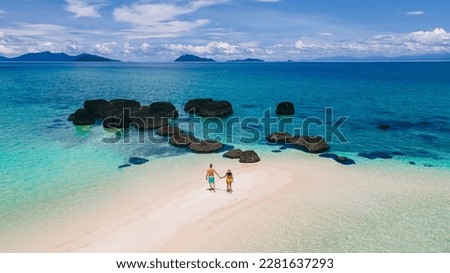 couple walking at the beach of Koh Kham Trat Thailand, aerial view of the tropical island near Koh Mak Thailand. white sandy beach with palm trees and big black boulder stones in the ocean