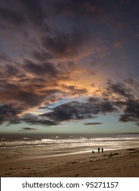 Couple Walking Dog On Beach At Sunset