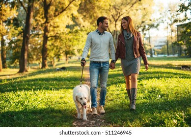 Couple Walking The Dog Together In The Park.