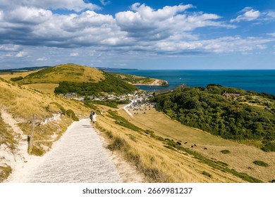 Couple walking down a hillside path towards the village and bay of Lulworth Cove.