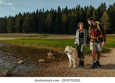 A couple walking hand in hand along a lakeside path with their dog. The scene is set in a lush, green forest with a clear blue sky. - Powered by Shutterstock