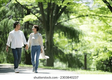 A couple walking hand in hand in fresh green in the light, gazing at each other, wide angle, with space for photocopying - Powered by Shutterstock