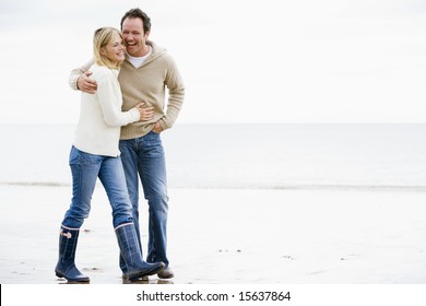 Couple walking on beach arm in arm smiling - Powered by Shutterstock