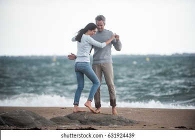 A couple are walking on the beach, they are barefoot and wear sweaters and jeans