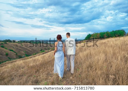 Couple walking on hill and field in the summer. Rear view