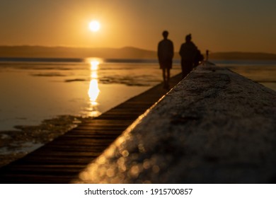 A Couple Walking On A Jetty Into The Sunset