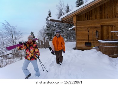 Couple Walking With Skis Outside Log Cabin