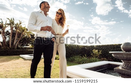 Couple walking together with wine in lawn of their house. Man and woman with a drink walking outdoors and having fun.