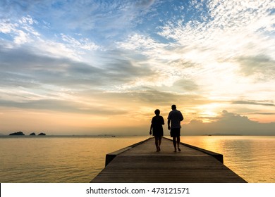 Couple walks along the pier at sunset over the sea - Powered by Shutterstock