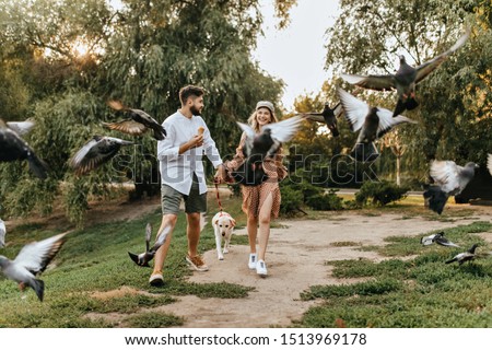 Couple walks in park with dog and scatters pigeons. Man eats ice cream and communicates with his wife during promenade
