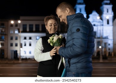 A couple walks through the city at night, the man presenting his wife with a bouquet of flowers - Powered by Shutterstock