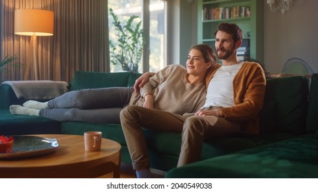 Couple Watches TV together while Sitting on a Couch in the Living Room. Girlfriend and Boyfriend embrace, cuddle, talk, smile and watch Television Streaming Services. Home with Cozy Stylish Interior. - Shutterstock ID 2040549038