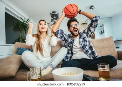 Couple is watching basketball game on the sofa at home.