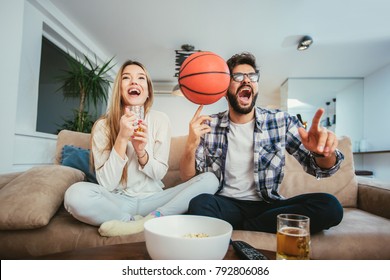 Couple Is Watching Basketball Game On The Sofa At Home.