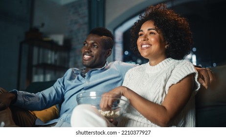 Couple Watching Comedy Movie on TV, Eating Popcorn while Sitting on Couch in the Apartment Late at Night. Laughing Boyfriend and Girlfriend Enjoying Funny TV Series at Home. Low Angle Shot. - Shutterstock ID 2210377927