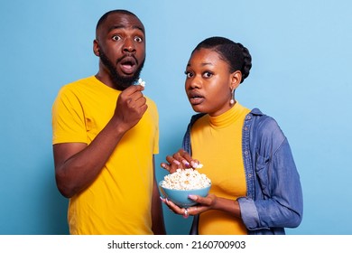 Couple Watching Horror Movie On Television And Eating Popcorn, Being Scared And Terrified To Watch Thriller Film In Studio. Frightened Boyfriend And Girlfriend Having Snack And Looking At Tv.