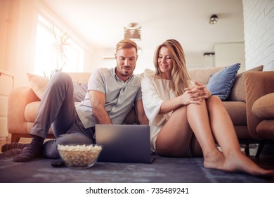 Couple Watching A Movie On Laptop In Their Living Room.Love, Technology, Internet And People Concept.