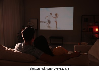 Couple watching movie on sofa at night, back view
