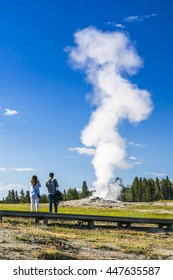 A Couple Watching On  Old Faithful In The Morning,summer, In Yellowstone National Park,usa.