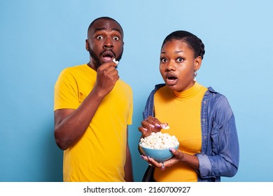 Couple Watching Scary Movie On Tv And Eating Popcorn, Being Scared And Terrified To Watch Thriller Film In Studio. Frightened Boyfriend And Girlfriend Having Snack And Looking At Television.