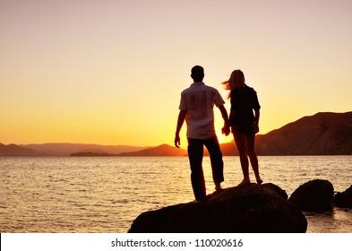 couple watching the sun by the sea while standing on a rock