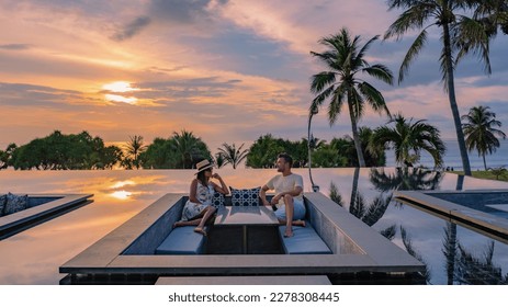 couple watching the sunset in an infinity pool on a luxury vacation in Thailand, man and woman watching the sunset on the edge of a pool in Thailand on vacation - Powered by Shutterstock