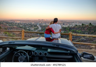 Couple watching sunset from popular view point in Los Angeles, California. Sitting on the sport convertible car hood