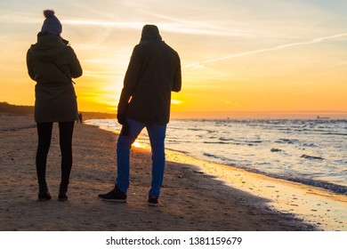 Couple Watching Sunset In Winter Day At The Seashore Of Riga Gulf, Baltic Sea, Vecaki, Latvia