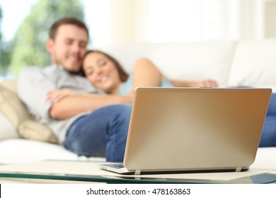 Couple watching tv in a laptop lying on a couch at home