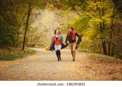 Couple weared in autumn-style clothes (oranfe scarf and vest) running through the autumn landscape. Alley covered with yellow foliage. Autumn walk outdoors. Two lovers in autumn park. Romantic dating