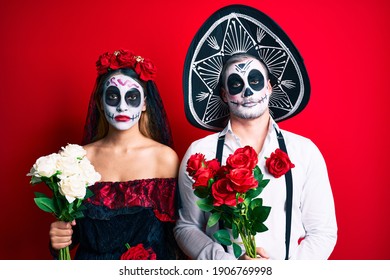 Couple Wearing Day Of The Dead Costume Holding Flowers Thinking Attitude And Sober Expression Looking Self Confident 