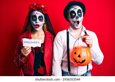 Couple Wearing Day Of The Dead Costume Holding Pumpking And Halloween Paper Afraid And Shocked With Surprise And Amazed Expression, Fear And Excited Face. 