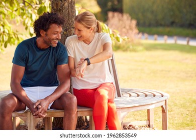 Couple Wearing Fitness Clothing Sitting On Seat Under Tree Checking Activity Monitor On Smartwatch - Powered by Shutterstock