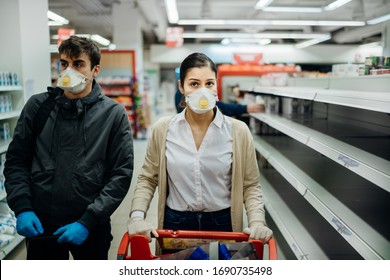 Couple Wearing Masks And Gloves Buying Groceries/supplies In Supermarket With Sold Out Products.Food Supplies Shortage.Empty Shelves Due To Coronavirus Covid-19 Outbreak Panic Buying And Hoarding.