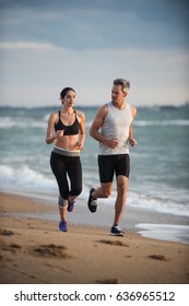 A couple wearing sportswear is running on the beach, the ocean at the background - Shutterstock ID 636965512