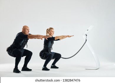 a couple wearing suits for electro muscle stimulation EMS performing squats. full length side view photo. copy space.family is fond of fitness