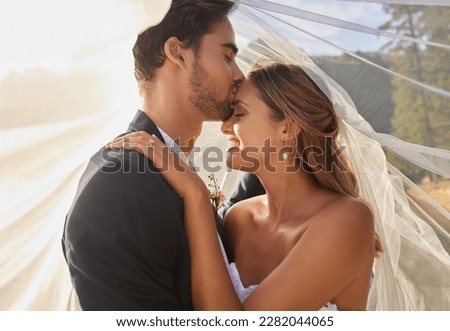 Couple, wedding and forehead kiss with vail for love, compassion or affection together in nature. Marred man kissing woman on head and hugging in marriage, relationship or loving embrace outdoors