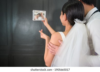 A Couple In Wedding Gown Are Making Video Call With Parents While Quarantine . Concept Of Wedding , Telecommunication , Covid-19 Prevention . 