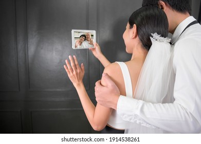 A Couple In Wedding Gown Are Making Video Call With Parents While Quarantine . Concept Of Wedding , Telecommunication , Covid-19 Prevention . 