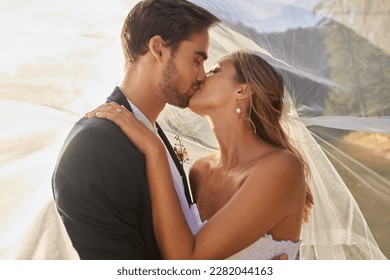 Couple, wedding and kissing with vail for love, compassion or affection together in nature. Married man kiss woman on lips, hugging in marriage, relationship or loving embrace for commitment outdoors