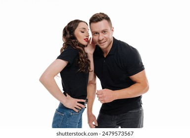 Couple Whispering Secret in Studio. A man and woman in black t-shirts stand against a white background - Powered by Shutterstock